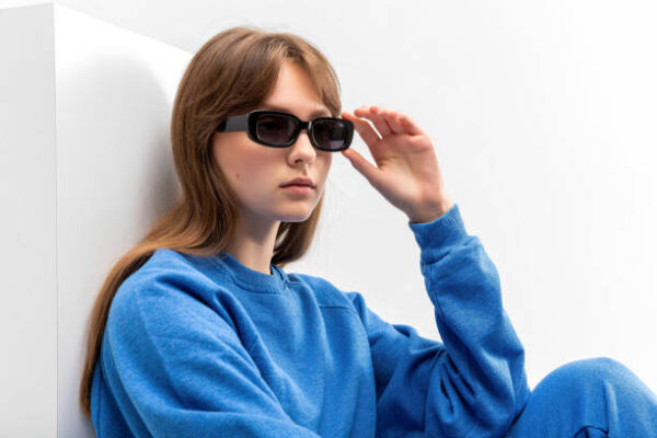 Young girl in blue tracksuit and black boots lying on cube isolated on white