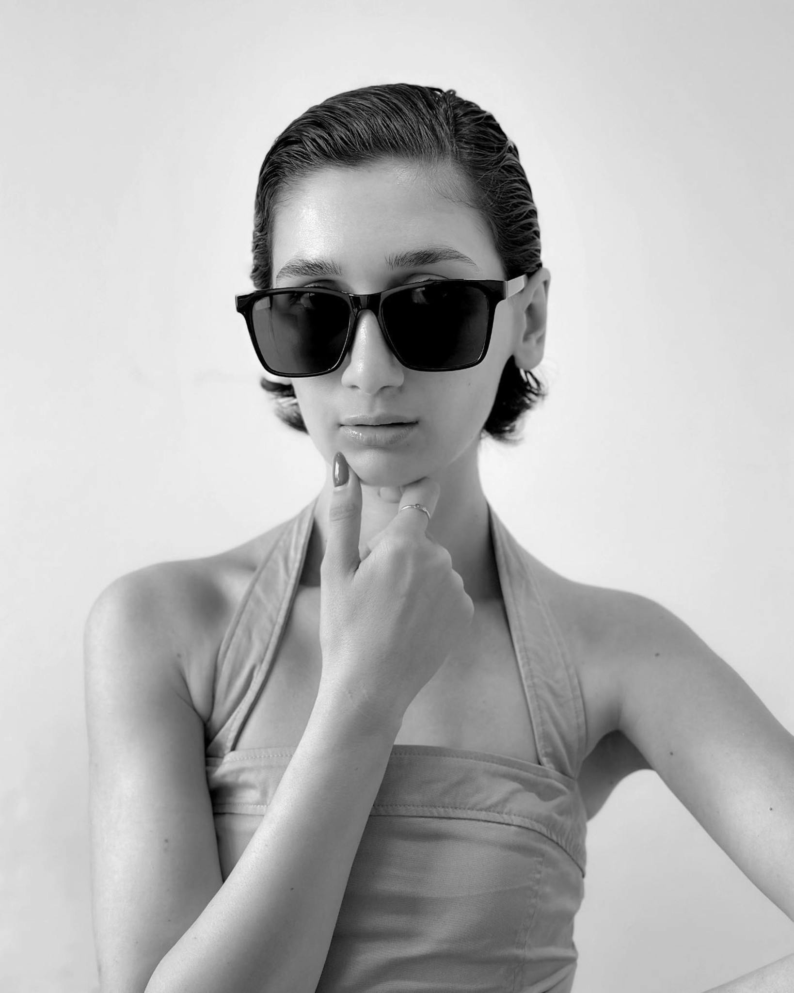 Chic black and white portrait of a woman wearing fashionable sunglasses indoors.