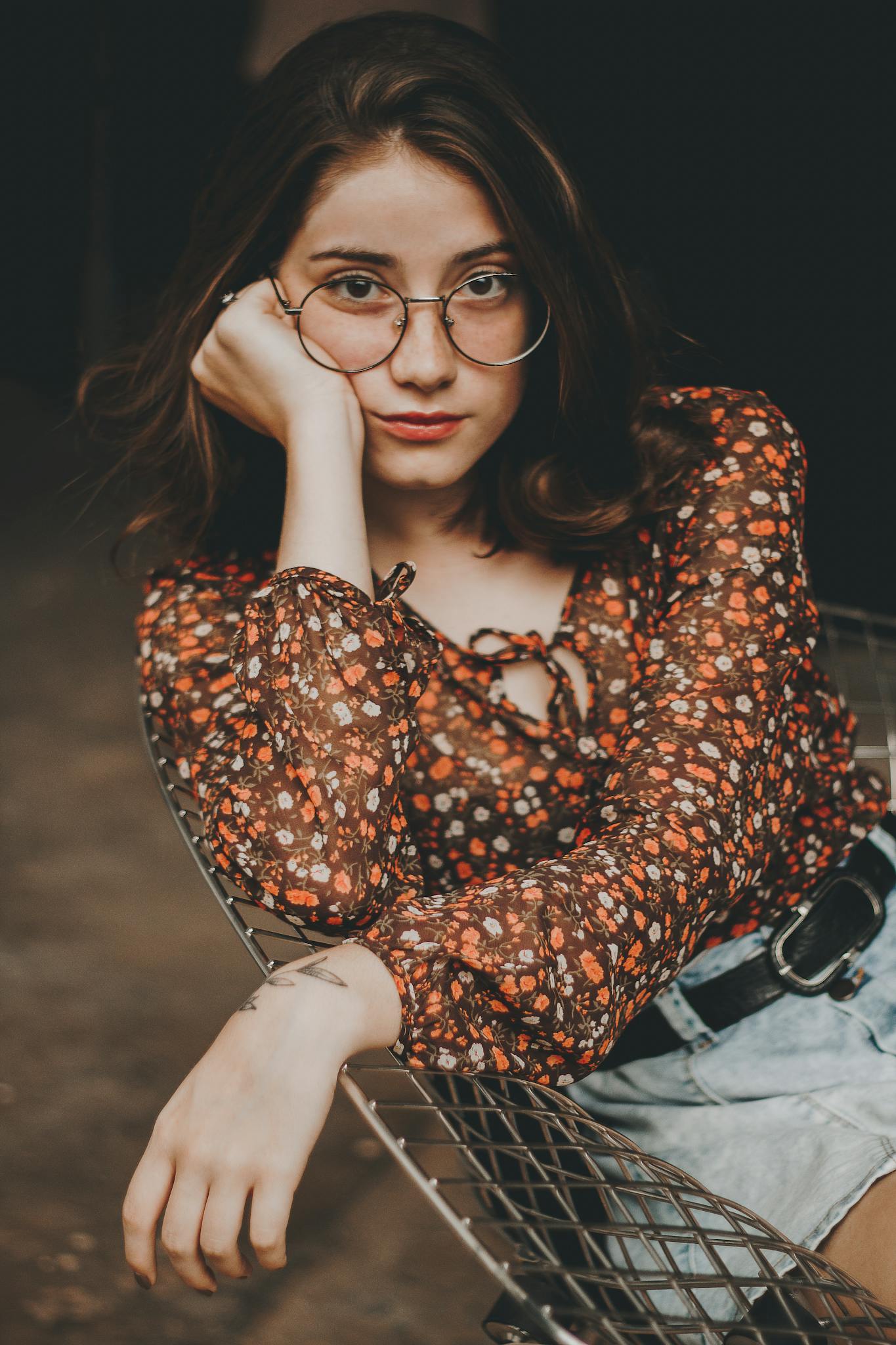 Confident young woman in floral top and glasses posing stylishly indoors.